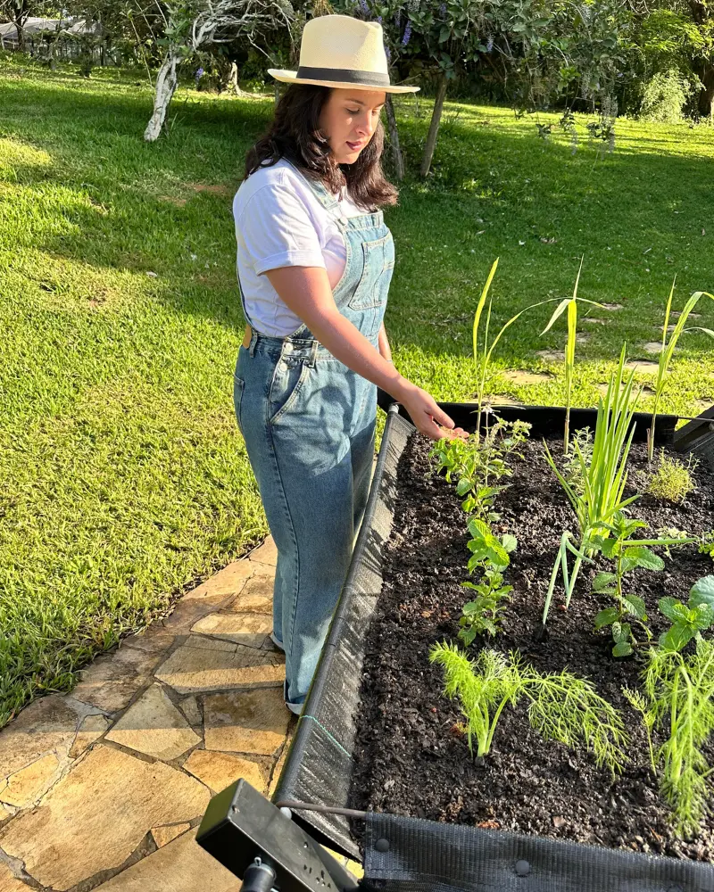 Mulher plantando temperos em horta vertical suspensa de alumínio.