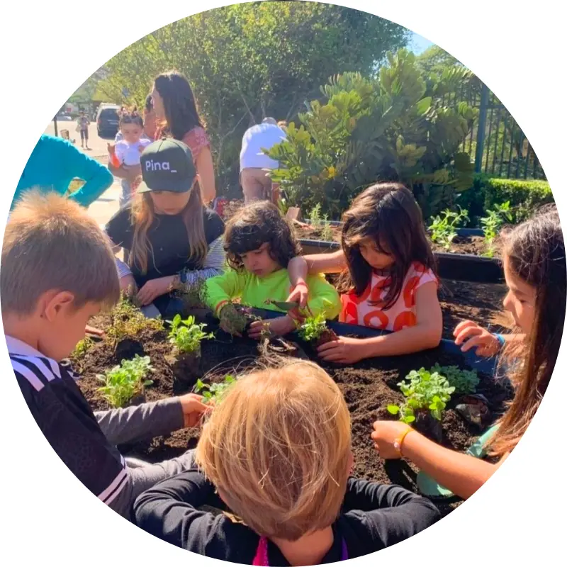 Crianças em um condomínio plantando hortaliças em canteiro de horta elevada.