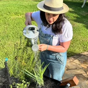 Mulher regando plantas com regador vintage de latão em horta suspensa de madeira.
