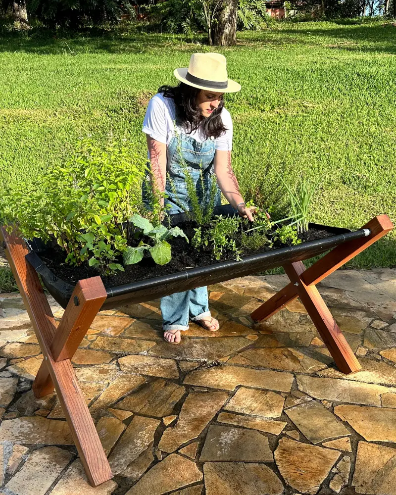 Mulher plantando temperos em canteiro elevado de horta em madeira
