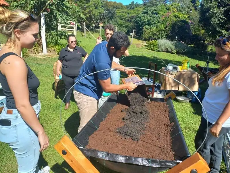 Homem despejando substrato orgânico de um balde em um canteiro elevado para preparar o solo para cultivo escolar.