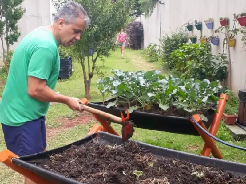 Homem realizando manutenção e revolvendo a terra em canteiro elevado de horta.