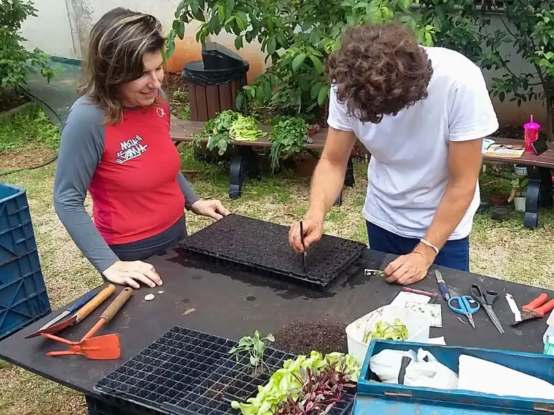 Especialista ensinando moradora a preparar bandejas de mudas durante oficina de horta.