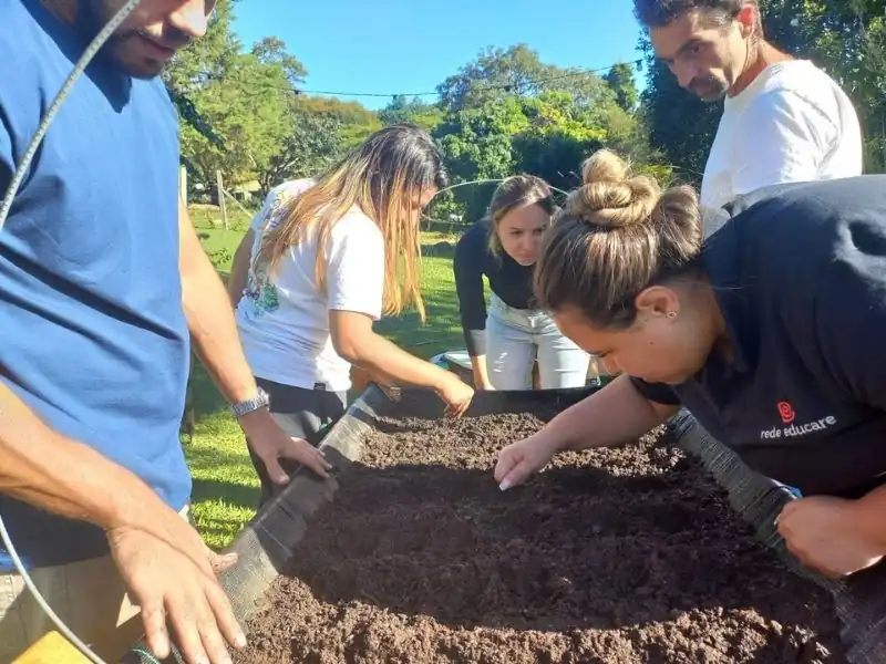 Grupo de pessoas ao redor de um canteiro elevado de madeira e lona preta, preparando a terra para o início do plantio.
