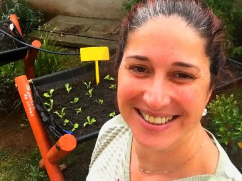 Selfie de moradora feliz em frente aos canteiros de horta no condomínio.