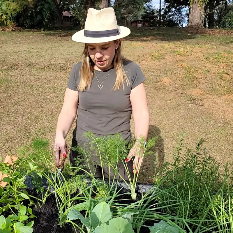 Mulher cuidando da horta suspensa do Jardim de Comer, organizando mudas e temperos no canteiro elevado para horta em casa.