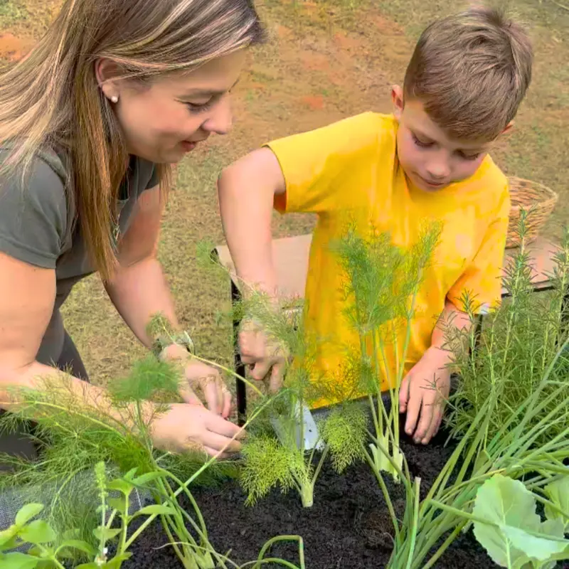 Mulher e criança plantando juntas em um cantinho de ervas e temperos, com uso prático e momento de convivência ao ar livre.