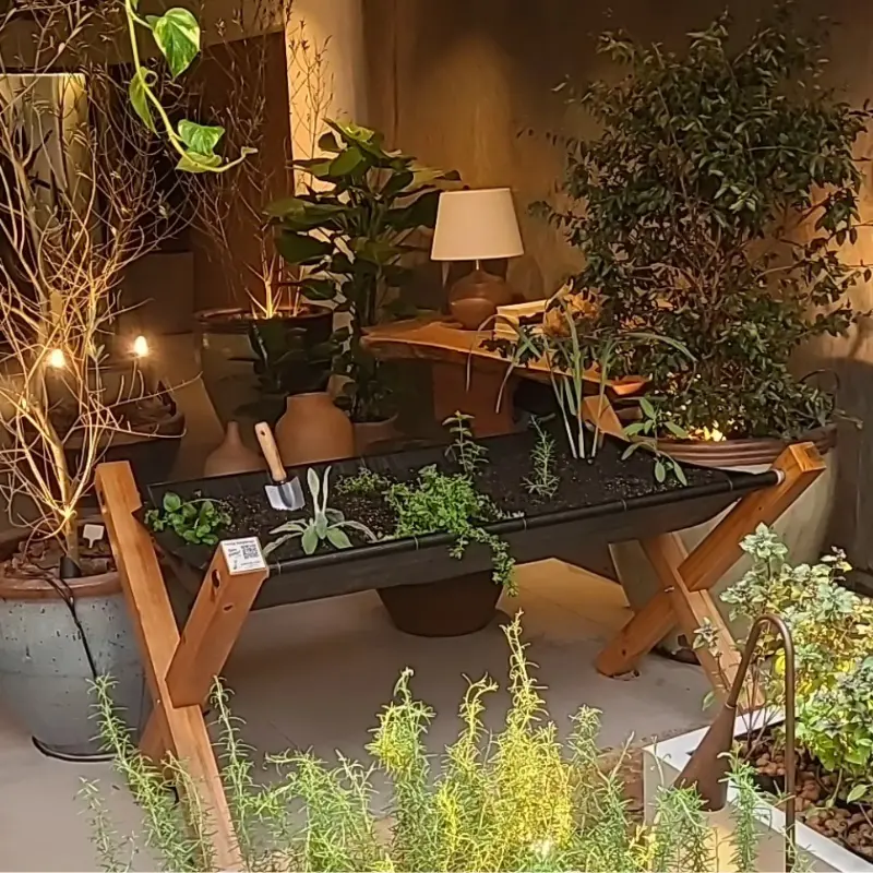 Cantinho de ervas e temperos integrado a um ambiente acolhedor, com iluminação quente e composição decorativa, em exposição de arquitetura e decoração Casa Cor.